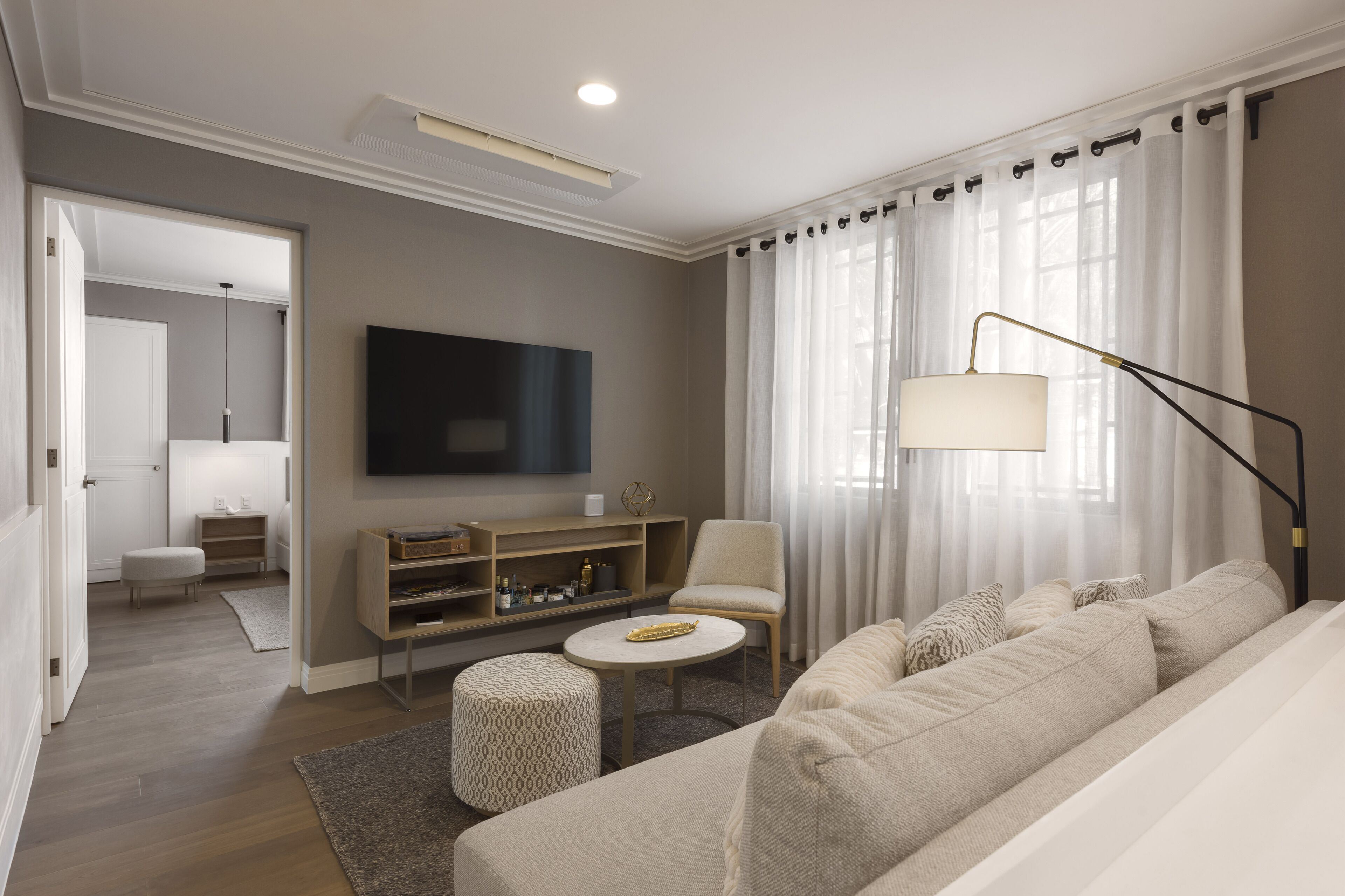 Et moderne hotelværelse med sofa, skammel, fjernsyn og lampe.