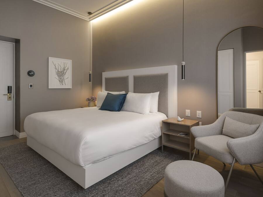 Una habitación de hotel moderna con una cama grande, una mesita de noche, una silla y un espejo.