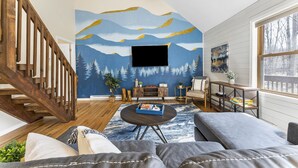 Un salon avec un escalier en bois, un téléviseur à écran plat fixé au mur, une table basse ronde avec un plateau et un canapé.
