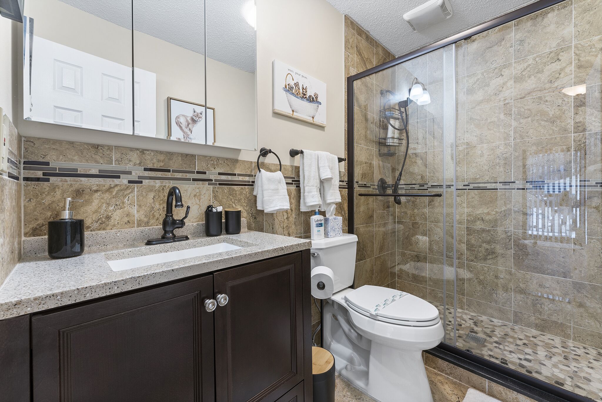 Een moderne badkamer met een douchecabine van glas, een wit toilet en een donker houten wastafelmeubel met een wastafel en spiegel.