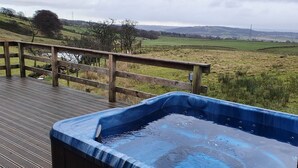 Una terraza de madera con un jacuzzi que da a un campo cubierto de césped.