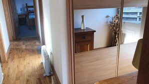 Pasillo con suelo de madera, un radiador y una puerta corredera con una pequeña mesa y un florero.