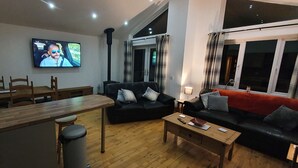 Una sala de estar moderna con una mesa de comedor de madera, un sofá de cuero negro y un televisor montado en la pared.