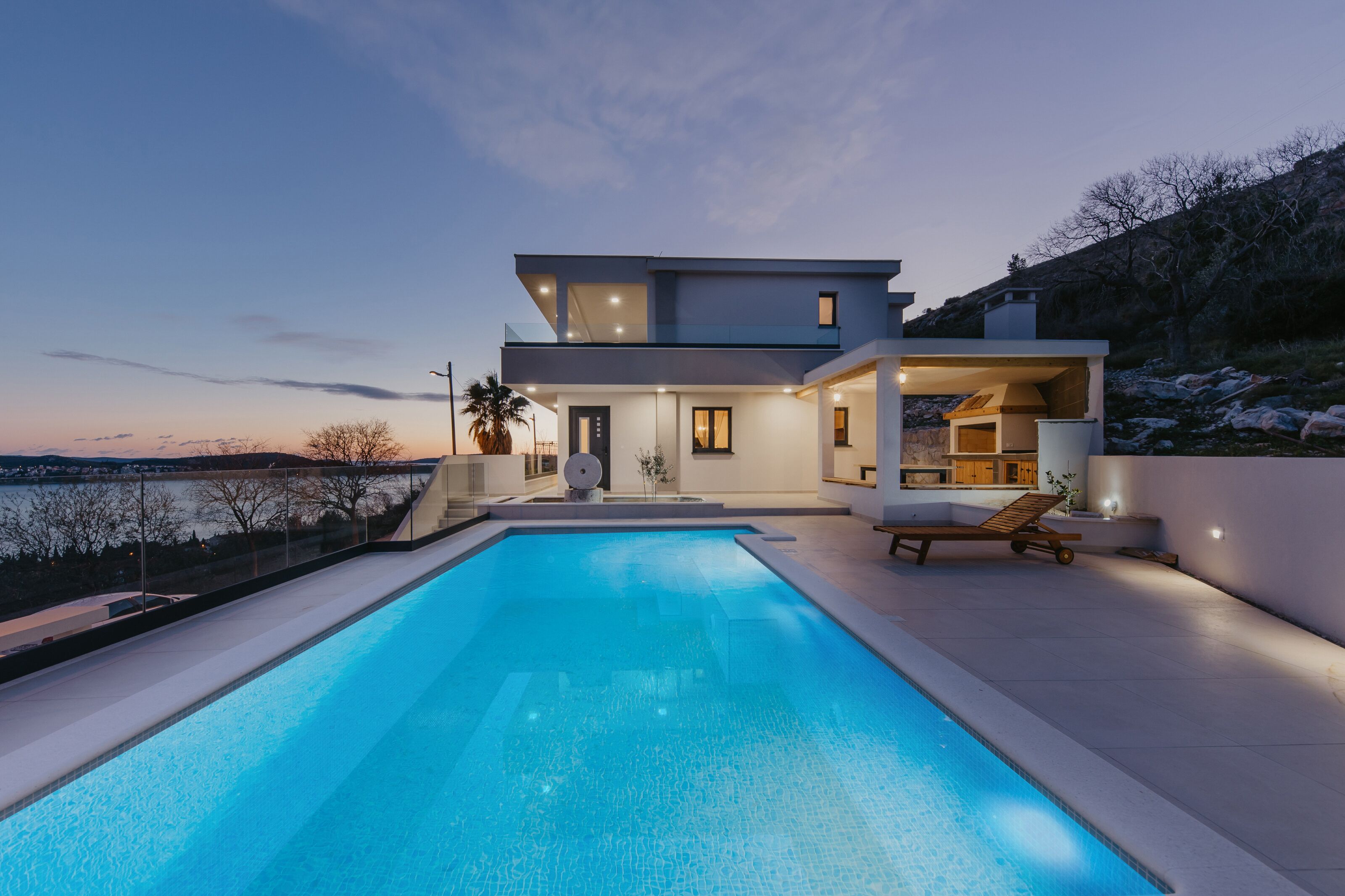 A modern two-story house with a swimming pool, a balcony, and a view of the water.