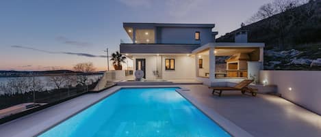 A modern two-story house with a swimming pool, a balcony, and a view of the water.
