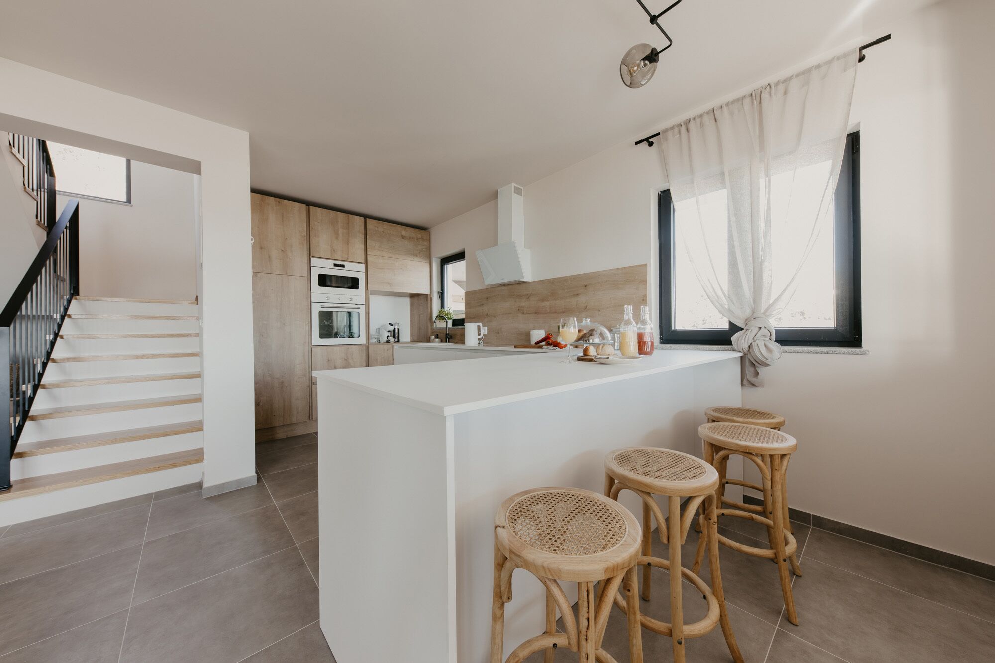 Una cocina moderna con una isla central, armarios de madera y una escalera.