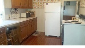 A kitchen with wooden cabinets, a white refrigerator, and a stove. - Aunt Jane's Yellow House downtown Great for Events (Put-in-Bay)