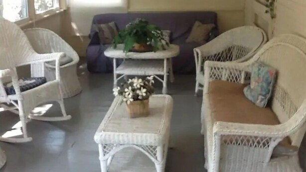 A cozy room with wicker furniture, including a sofa and chairs, a small table with a plant, and a window providing natural light. - Aunt Jane's Yellow House downtown Great for Events (Put-in-Bay)
