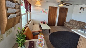 A cozy living room with a wooden bench, a sofa, a dining table, and a ceiling fan. - OYO Sandman Inn (Eagle Grove)