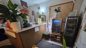 A reception area with a wooden counter, a plant, a welcome sign, an ATM, and a small table with a tray of snacks. - OYO Sandman Inn (Eagle Grove)
