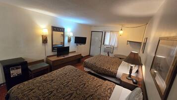 Une chambre d’hôtel avec deux lits, un bureau avec une télévision, un miroir et une petite table avec une lampe.