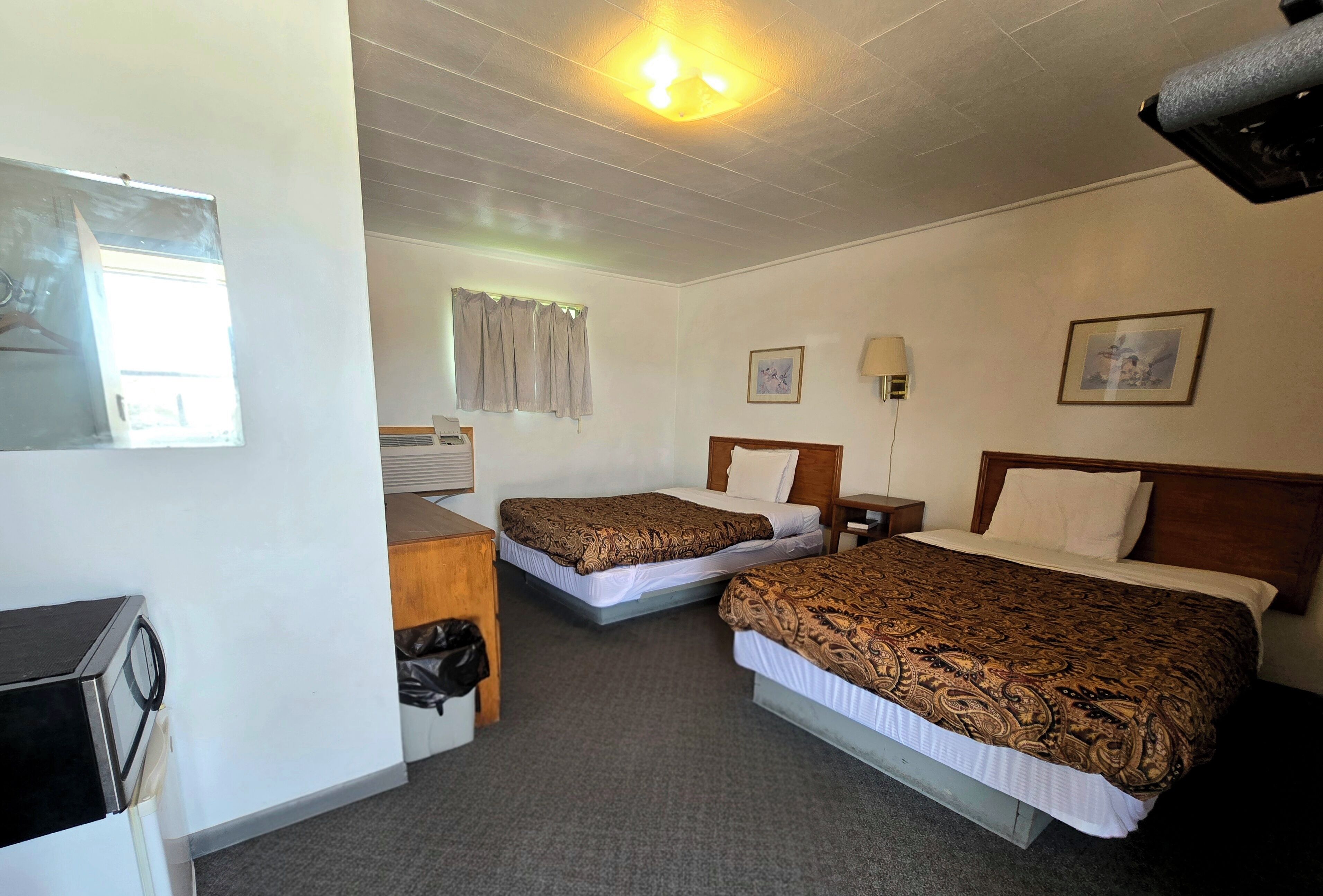 Ett hotellrum med två sängar, ett skrivbord, en stol, en bordslampa och en taklampa.