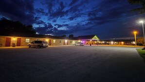 A motel with a large parking lot, a central building with a neon sign, and a well-lit exterior. - OYO Sandman Inn (Eagle Grove)