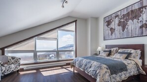 Un dormitorio con un ventanal grande, una cama con ropa de cama estampada, un mapa mundial en la pared y una silla.