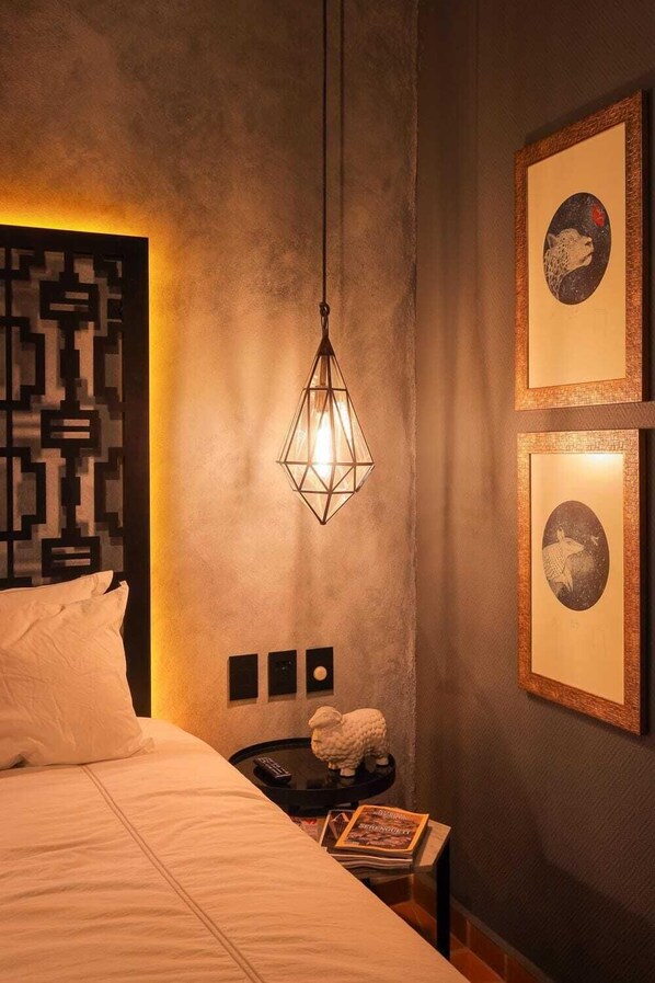Habitación de hotel con cama, mesita de noche, lámpara de pared y cuadros enmarcados.