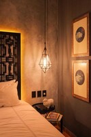 Habitación de hotel con cama, mesita de noche, lámpara de pared y cuadros enmarcados.
