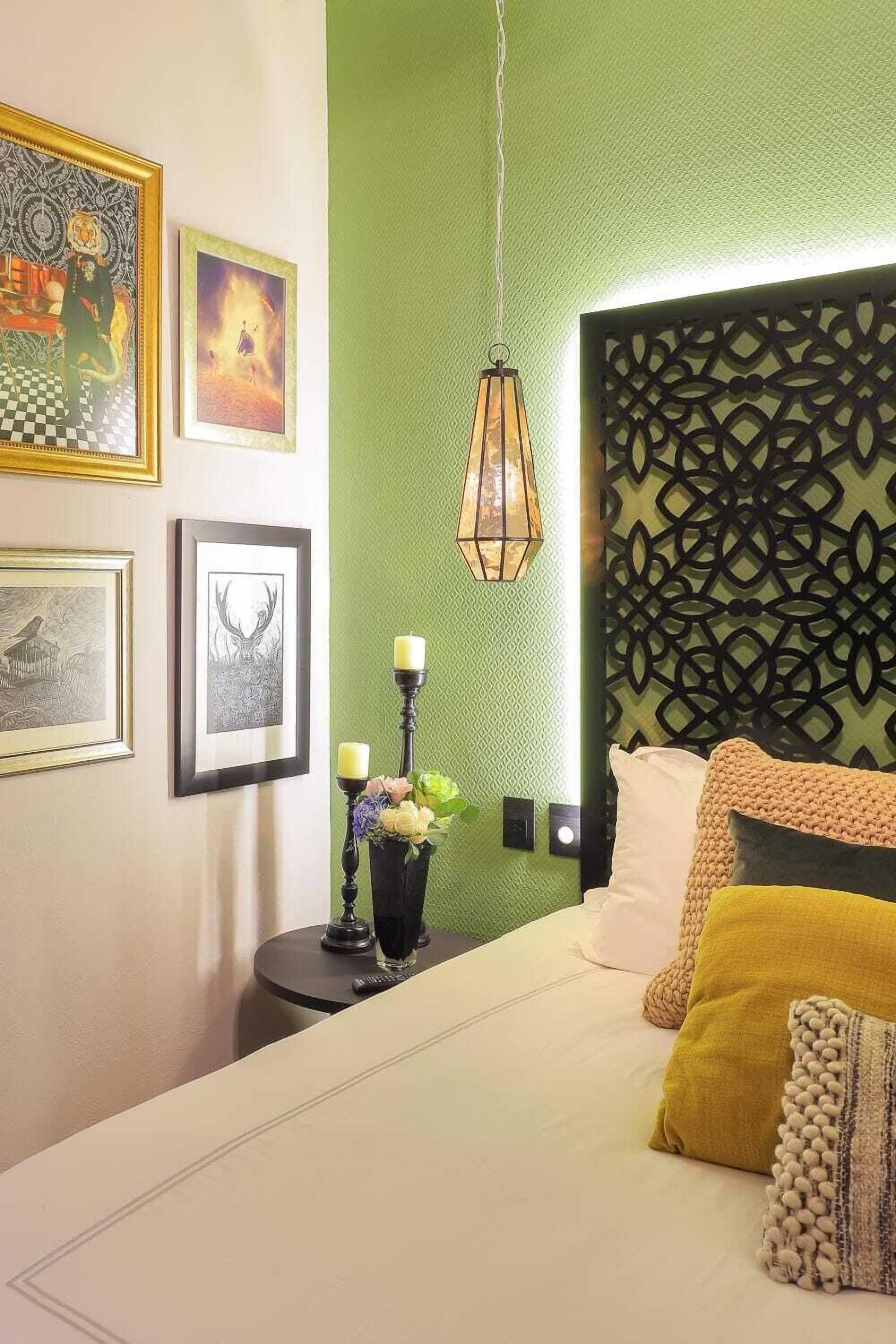 A bedroom with a green accent wall, a patterned headboard, and framed artwork on the wall.