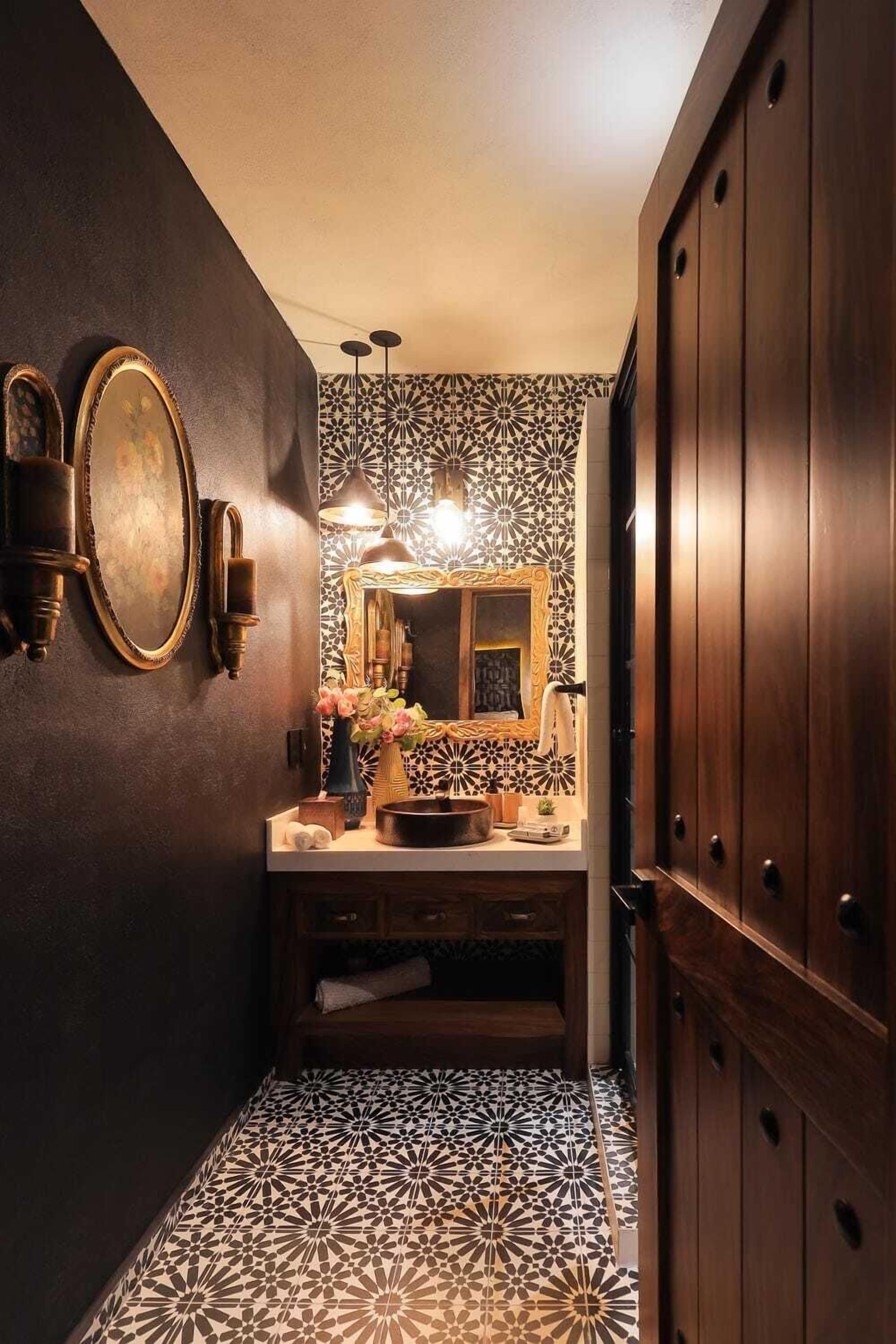 A bathroom with a dark wall, a patterned tile floor, a sink with a mirror, and a wooden cabinet.
