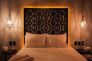 Un dormitorio con un cabecero estampado, dos mesitas de noche con objetos decorativos y una cama con ropa de cama blanca.