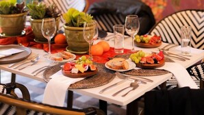 Une table à manger dressée avec des assiettes remplies de nourriture, des verres et des plantes en pot.