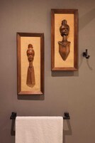 Dos esculturas de madera enmarcadas en una pared, una toalla colgada en un perchero debajo.