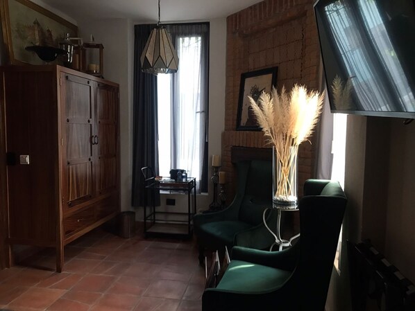 A living room with a wooden cabinet, a green armchair, a table with a vase of pampas grass, and a fireplace. - Hotel Casamada (San Miguel de Allende)