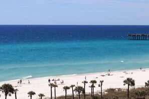 A beach with a pier extending into the ocean, palm trees in the foreground, and people enjoying the beach. - Winter Paradise-Corner Unit Panoramic Sunsets–3BR/3BA + Bunk–Sleeps 10 (Panama City Beach)