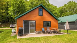A wooden cabin with a green roof, a sliding glass door, and a patio area with outdoor furniture. - Cabin with private dock and large yard space! (Butternut)