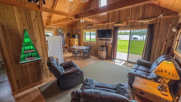 A cozy cabin interior with a fireplace, leather seating, a dining area, and a view of the outdoors. - Cabin with private dock and large yard space! (Butternut)