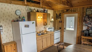 A kitchen with wooden cabinets, a refrigerator, a stove, and a sink. There is a clock on the wall and a door with a sign above it. - Cabin with private dock and large yard space! (Butternut)