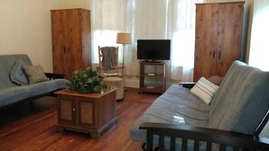 A living room with a grey sofa, a wooden cabinet, a television on a stand, and a small table with a plant. - Aunt Jane's #1 Downtown Put in Bay up to 12 guests (Put-in-Bay)