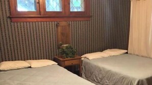 A room with two beds, a wooden nightstand with a plant, a window with curtains, and a striped wall. - Aunt Jane's #1 Downtown Put in Bay up to 12 guests (Put-in-Bay)