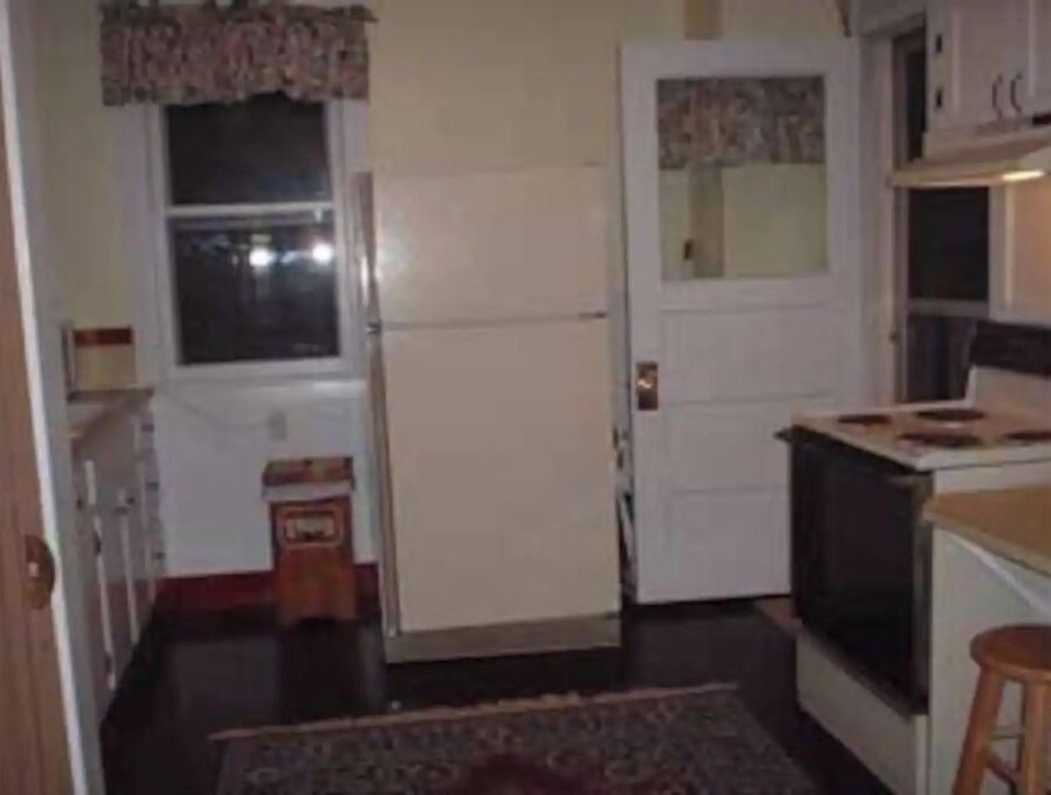 A compact kitchen with a refrigerator, stove, and a small wooden stool.