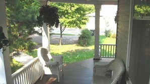 A covered porch with wicker furniture and hanging plants. - Aunt Jane's #1 Downtown Put in Bay up to 12 guests (Put-in-Bay)