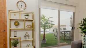 Ein modernes Wohnzimmer mit einem gelben Bücherregal, einem großen Fenster mit Blick auf eine Terrasse und einem grauen Sofa.