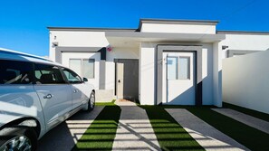 A modern two-story house with a white exterior, a driveway with artificial grass, and a parked white car.