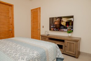 A bedroom with a bed, a wooden wardrobe, a TV on a wooden stand, and a small plant. - Brand New Home Heated Pool By FMI Rentals (Puerto Peñasco)