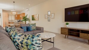 Ein modernes Wohnzimmer mit grauem Sofa, gemusterten Kissen, einem runden Couchtisch und einem flachbildfernseher, der an der Wand angebracht ist.
