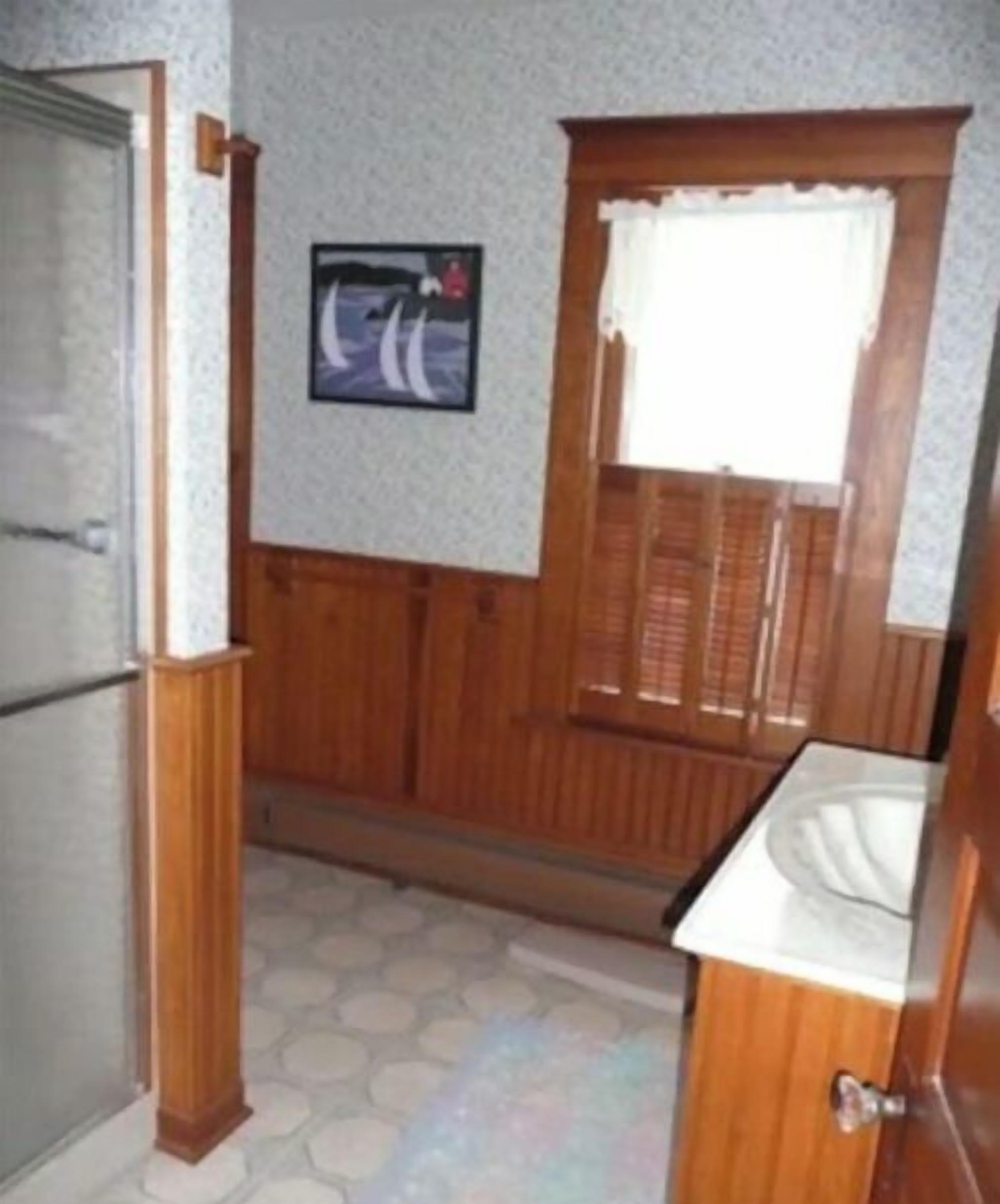 A bathroom with a wooden vanity, a sink, a window with wooden shutters, and a framed picture on the wall.