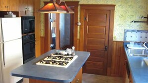Una cucina compatta con isola centrale, frigorifero, forno, lavello e una lampada decorativa a sospensione.
