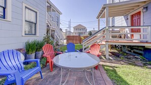 Eine Terrasse mit einem runden Tisch und vier Adirondack-Stühlen, umgeben von einer Holzterrasse und einem kleinen Garten.
