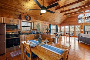 Une cuisine spacieuse équipée d’appareils modernes, un coin repas avec une table en bois et un salon confortable avec un canapé et de grandes fenêtres.
