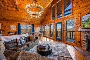 Un intérieur de chalet chaleureux avec un grand plafond en bois, une cheminée, un canapé et un coin repas.