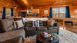 Een gezellig interieur van een chalet met een grote leren bank, een eettafel en een keukenhoek.