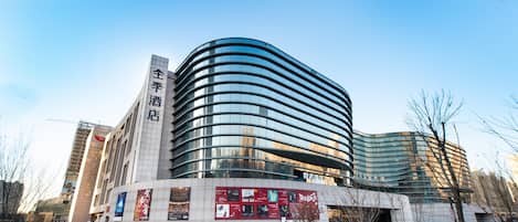 Un bâtiment moderne doté d’une façade en verre incurvée, d’une enseigne bien visible sur le côté gauche et d’un espace de stationnement au premier plan.
