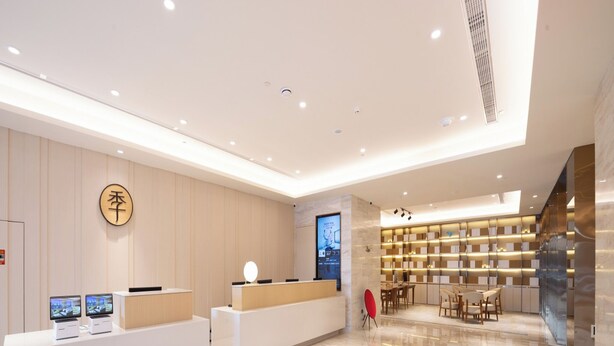 A modern hotel lobby with a reception desk, a digital display, a seating area, and a wall-mounted bookshelf. - Ji Hotel (Shijiazhuang)