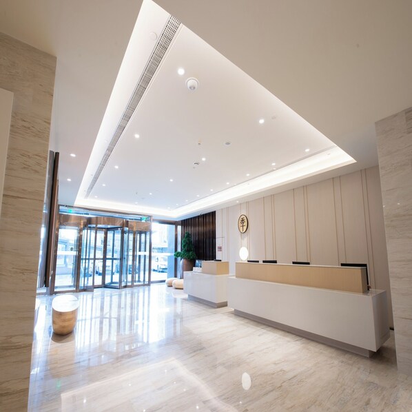 Un área de recepción moderna con entrada de vidrio, mostrador de recepción e iluminación empotrada en el techo.