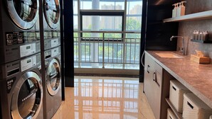 A modern laundry area with stacked washers and dryers, a large window with a view of buildings, and a kitchen area with a sink and storage shelves. - Ji Hotel (Shijiazhuang)