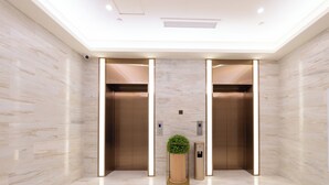 A modern elevator with a marble wall, a plant, and a trash bin. - Ji Hotel (Shijiazhuang)