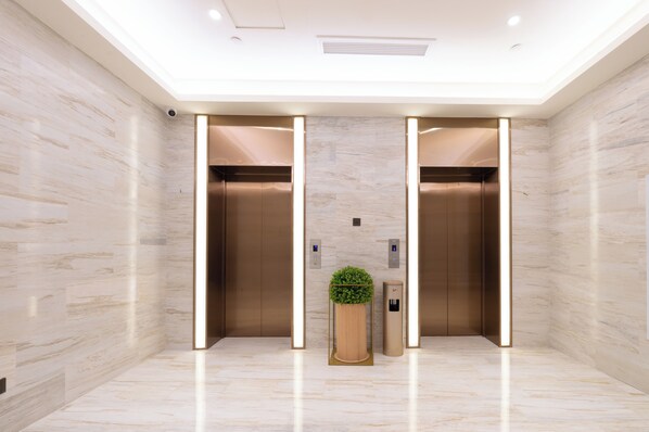 A modern elevator with a marble wall, a plant, and a trash bin.